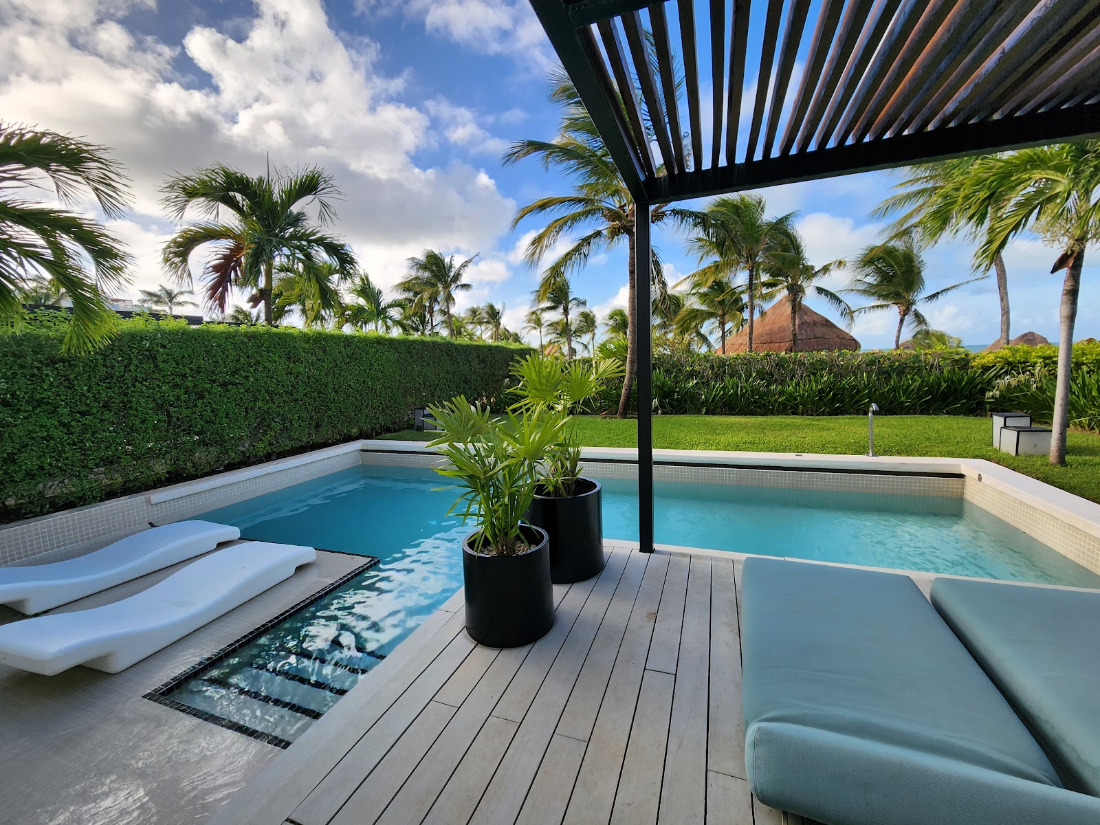 Private poolside cabana at Finest Playa Mujeres with loungers, black pergola, turquoise pool, and palm-lined grounds under blue sky.