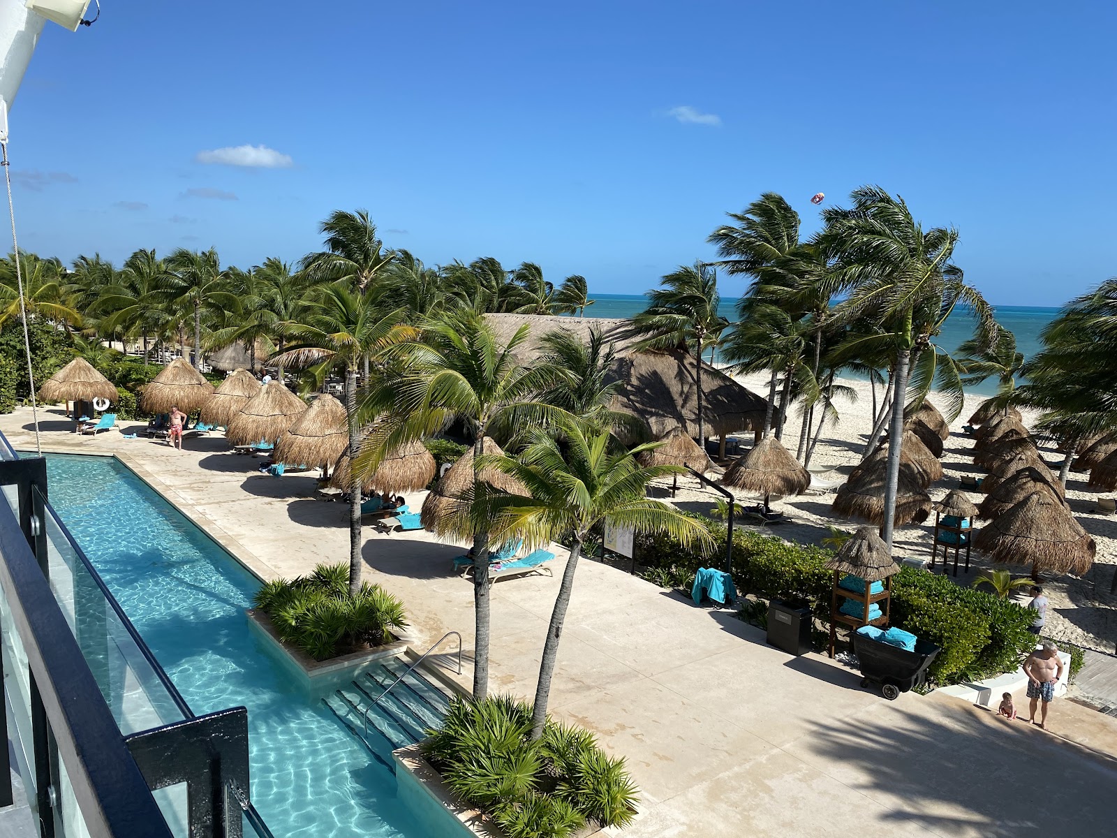 Finest Playa Mujeres pool deck with turquoise water, thatched palapas, palm trees, and white sand beach beyond under clear blue sky.