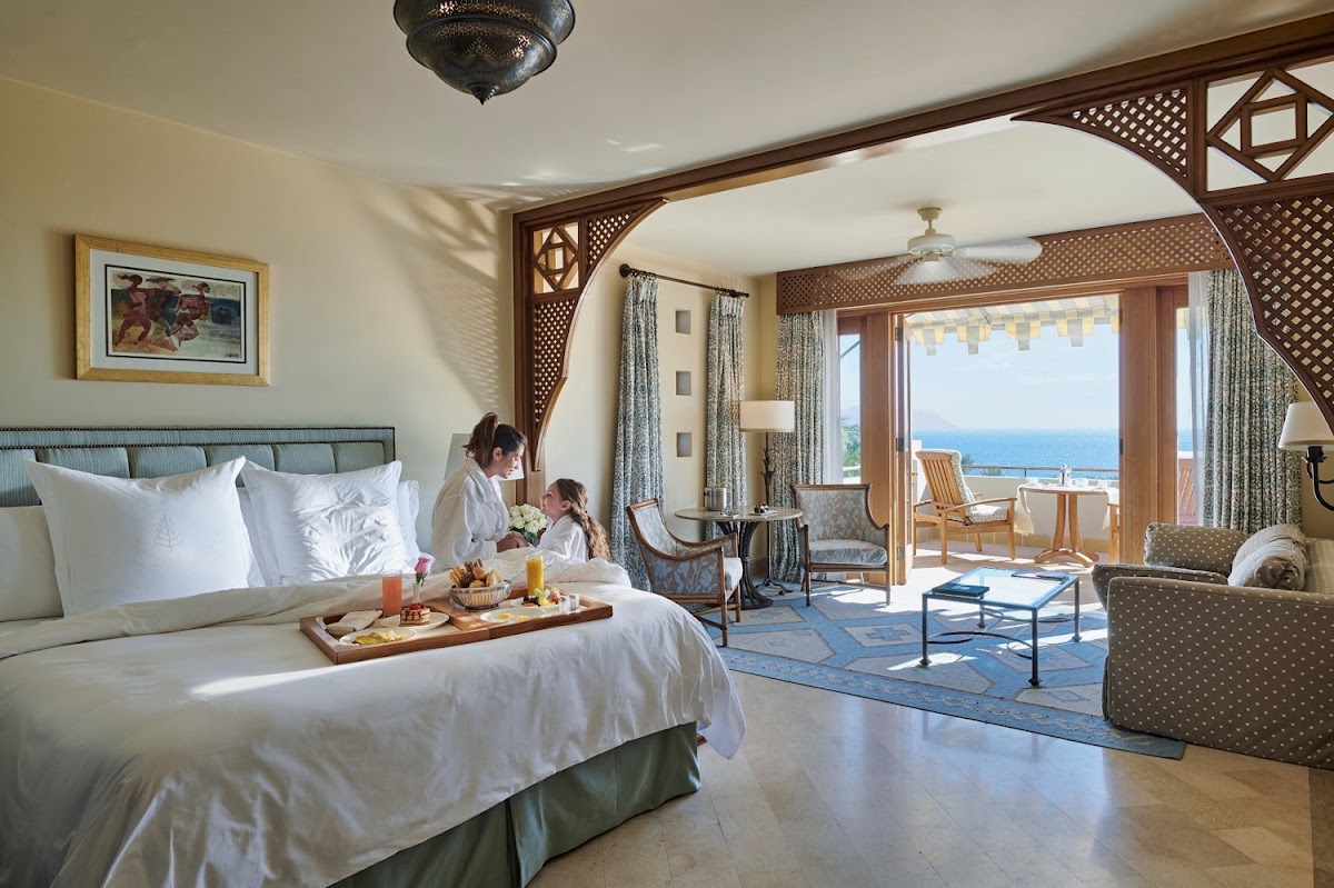 Spacious resort suite with a king bed, seating area, and ocean-view balcony overlooking the Red Sea and beach.