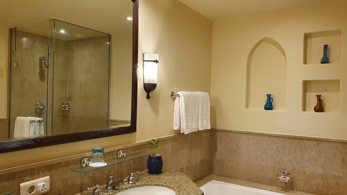 Bathroom with cream walls, granite countertop, glass shower enclosure, and decorative niches holding blue and amber vases.