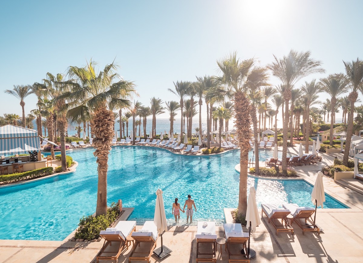 Large lagoon pool surrounded by palm trees with loungers and umbrellas, overlooking the Red Sea at Four Seasons Sharm el Sheikh.