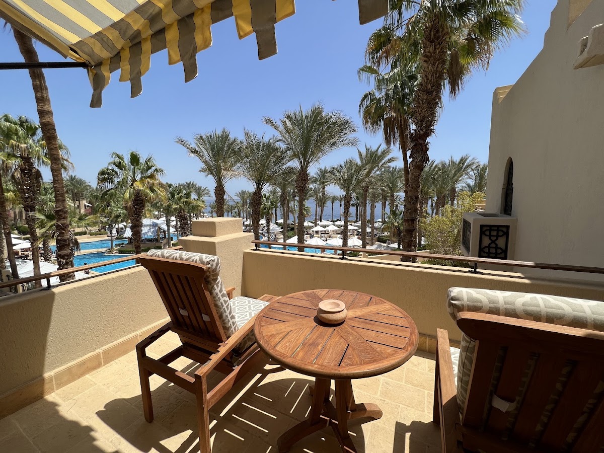 Private balcony with wooden furniture overlooking palm-lined grounds, pools, and sea at Four Seasons Sharm el Sheikh.