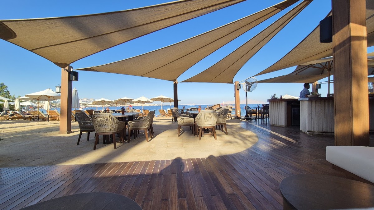 Shaded seating area with tan sail canopies overlooks a beach and blue bay at Four Seasons Sharm el Sheikh.