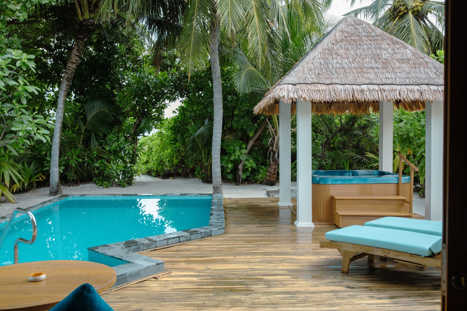 Private villa deck at Furaveri Maldives with turquoise plunge pool, loungers with cushions, white cabana, and palm trees framing ocean views.
