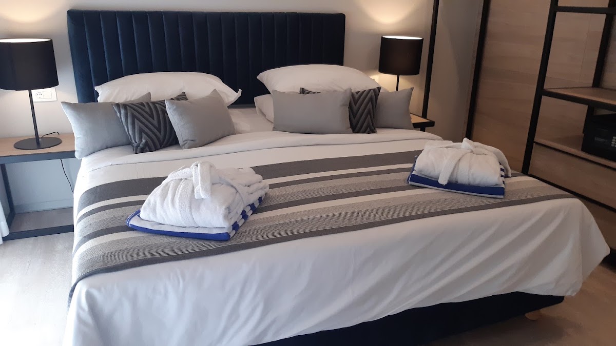 Resort bedroom with king bed, blue velvet headboard, white pillows and folded towels, nightstands with lamps, and wood paneling.