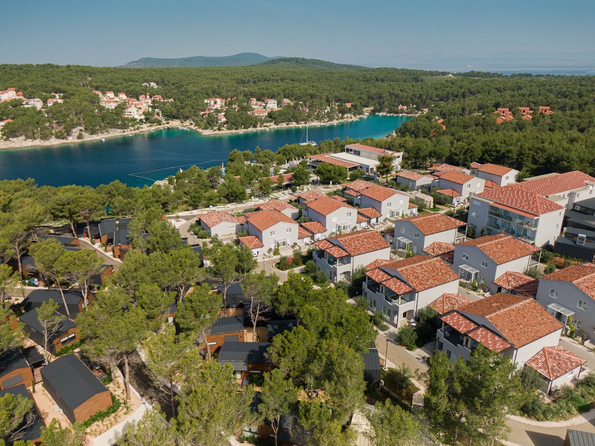 Aerial view of the Gava Waterman Milna Resort with terracotta-roofed cottages nestled among pine trees overlooking a turquoise cove.
