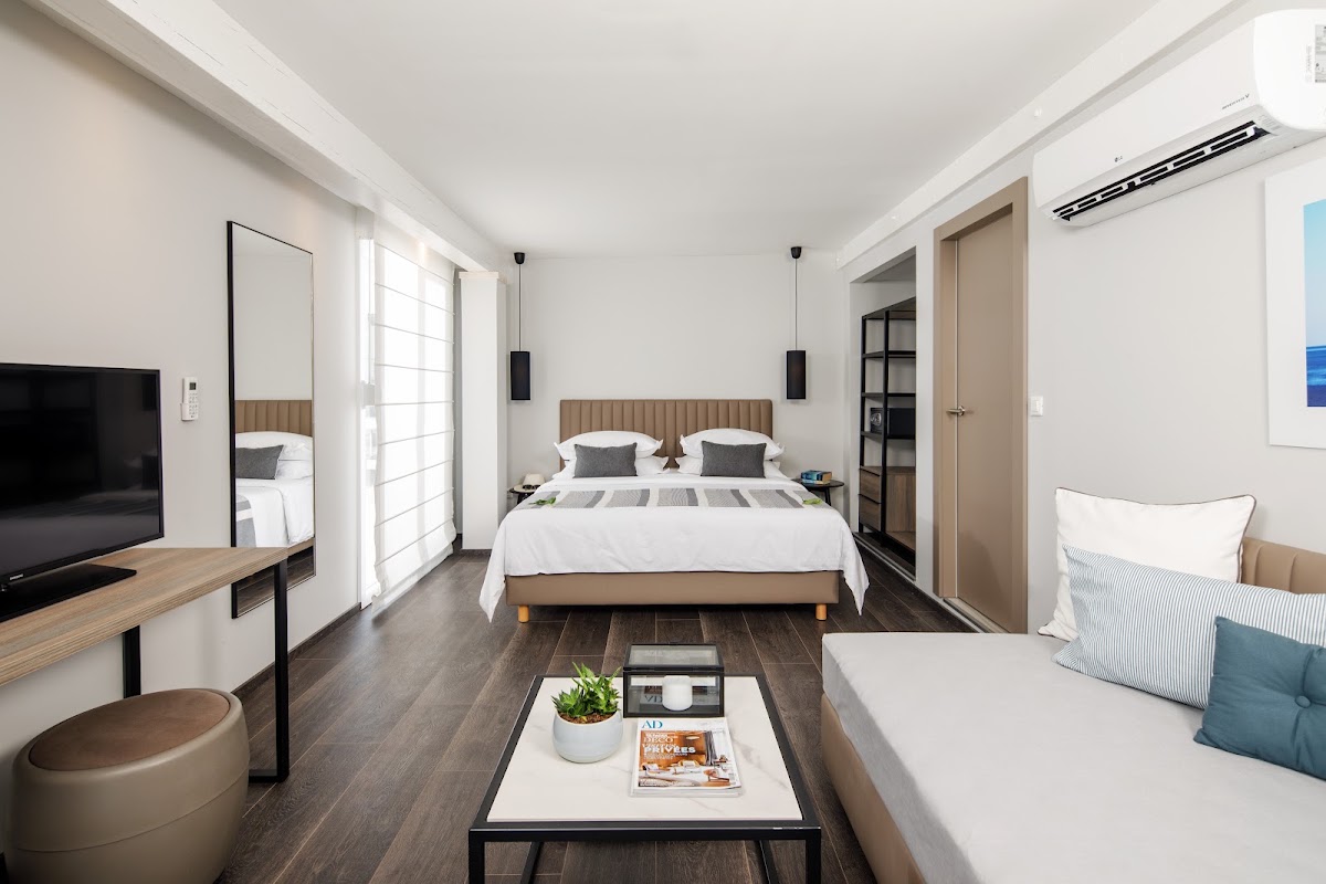 Modern resort room with queen bed, seating area, TV, and glass doors opening to a balcony with natural light.
