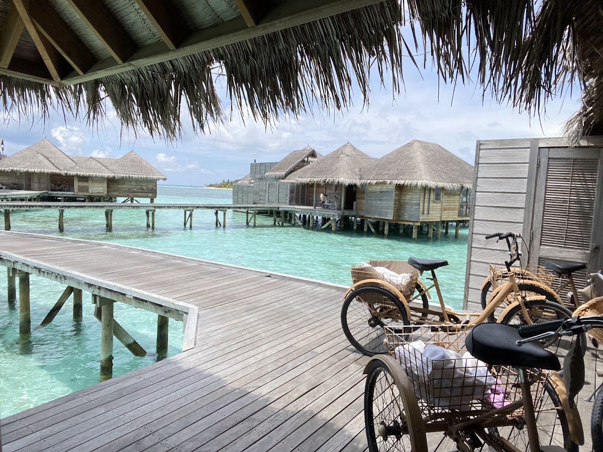 Bicycles on a wooden deck overlook thatched-roof overwater bungalows and turquoise lagoon at Gili Lankanfushi.