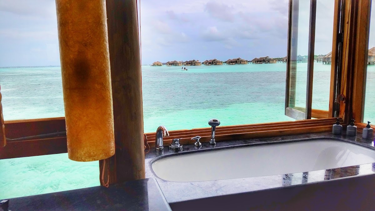 Bathroom with soaking tub and windows overlooking turquoise lagoon and overwater bungalows at Gili Lankanfushi.