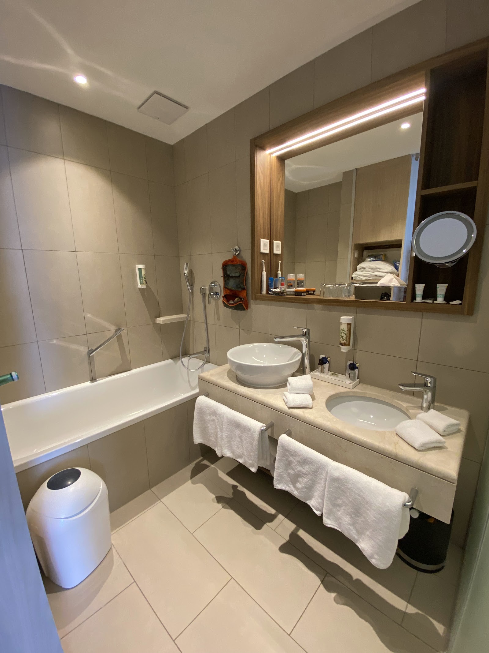 Modern bathroom with dual vessel sinks, lighted mirror, soaking tub with glass enclosure, and heated towel racks.
