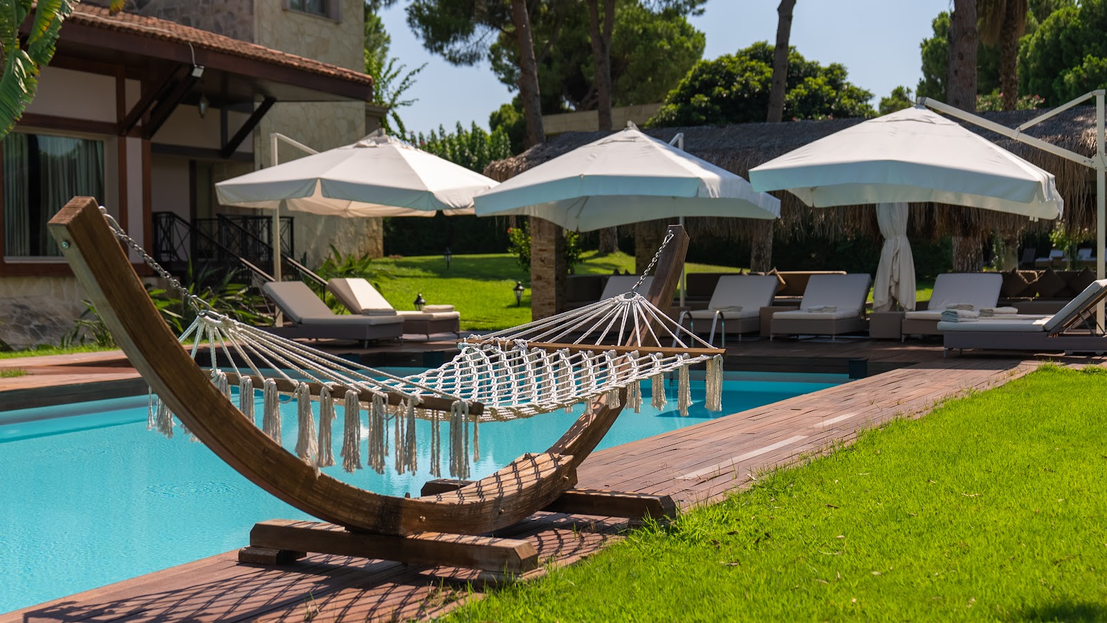 Wooden hammock suspended over turquoise pool with white umbrellas and lounge chairs lining the deck at Gloria Serenity Resort.