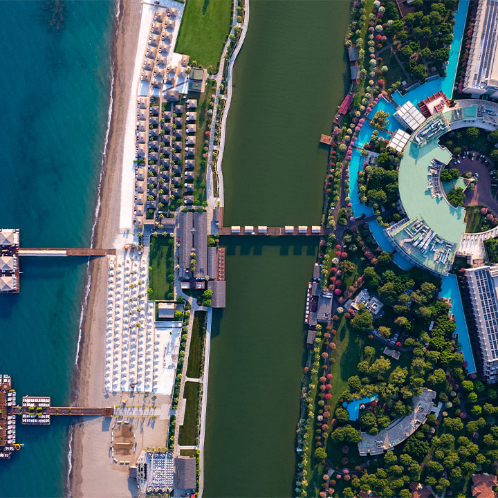 Aerial view of Gloria Serenity Resort with beachfront buildings on turquoise water and lagoon-side pools and grounds surrounded by trees.