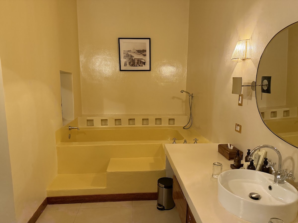 Pale yellow bathroom with a sunken tub, circular mirror, round white sink, and framed vintage photograph on the wall.