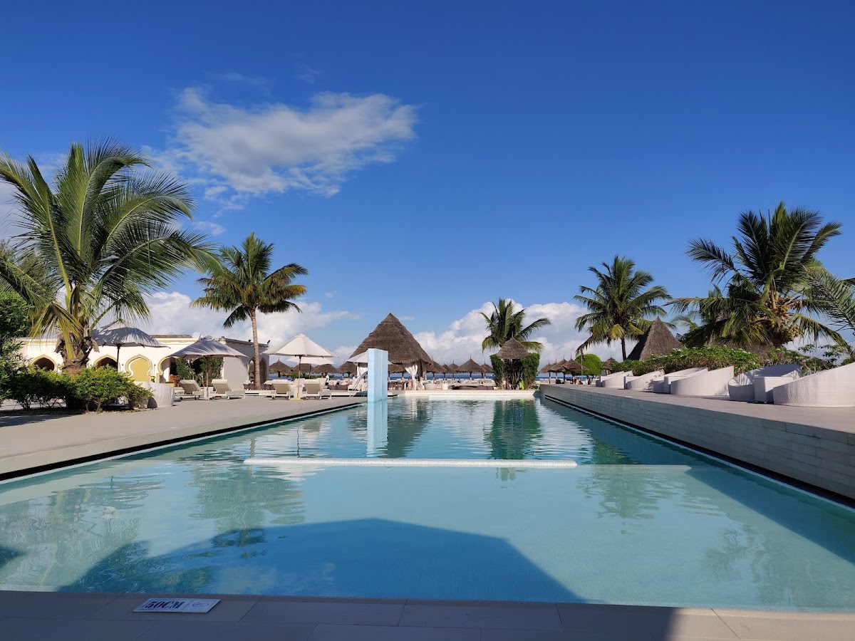 Linear pool with water feature overlooking palm-lined beach and thatched-roof buildings at Gold Zanzibar Beach House & Spa.