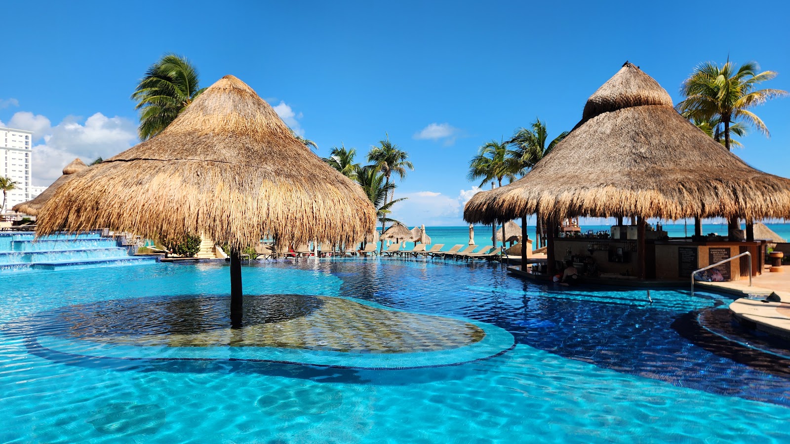 Indoor lap pool at Grand Fiesta Americana Coral Beach with turquoise water, symmetrical wooden columns, and lit ceiling in a modern spa facility.