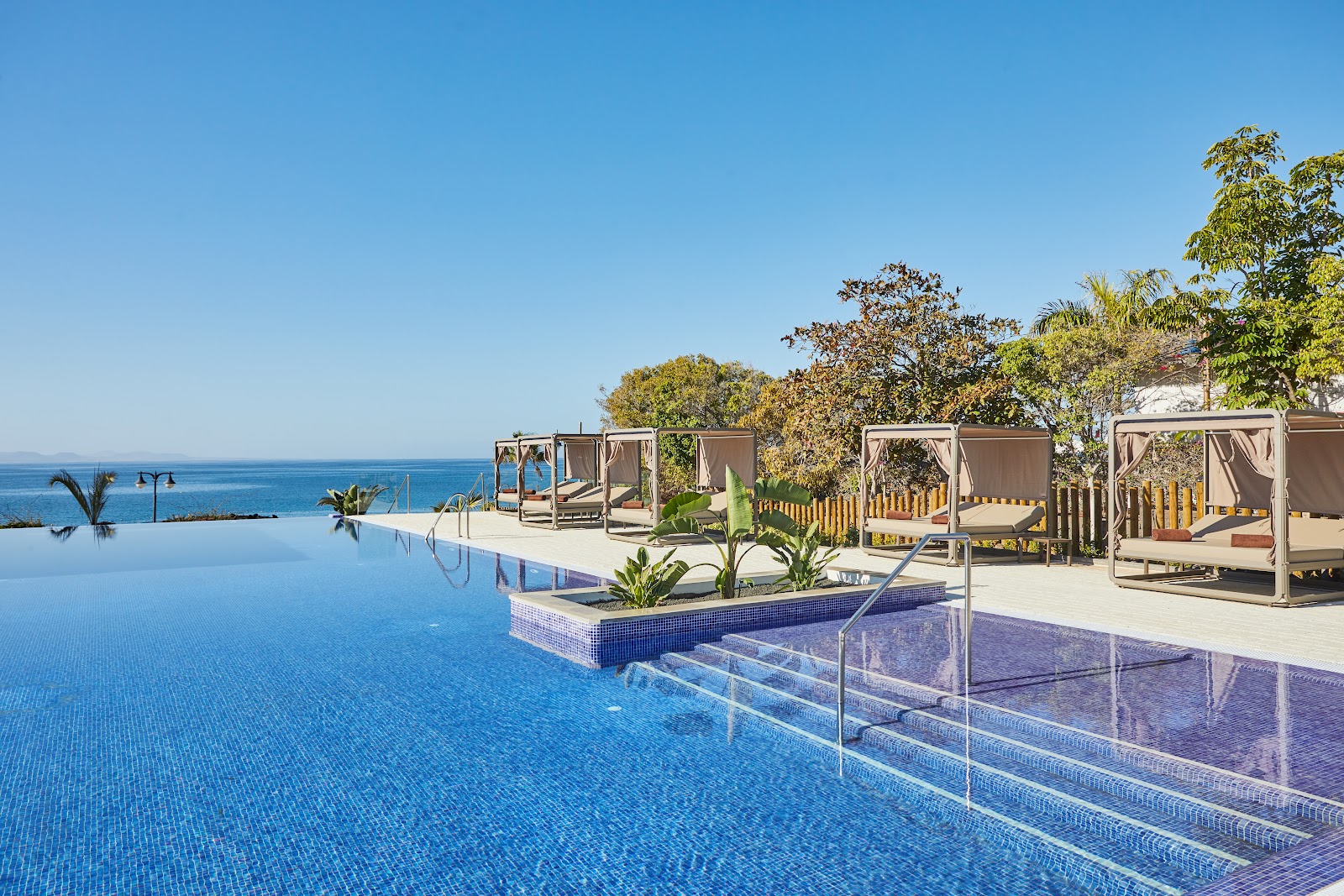 Infinity pool overlooking the ocean with cabanas, lounge chairs, and tropical plants at Grand Hyatt Lanzarote Playa Dorada Resort.