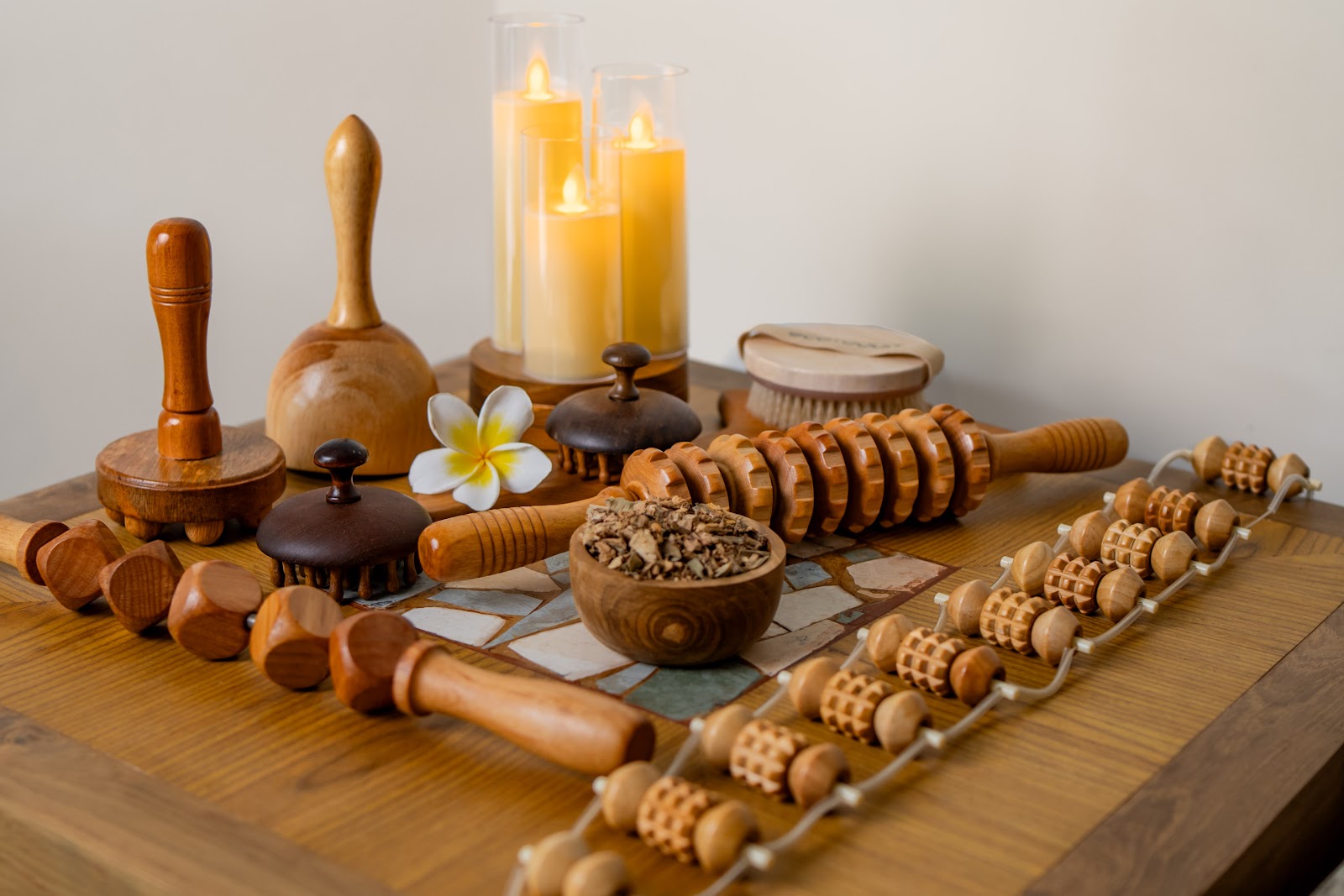 Spa treatment tools and wooden massage implements arranged on a table with candles and a white flower at Grand Mirage Resort & Thalasso Bali.