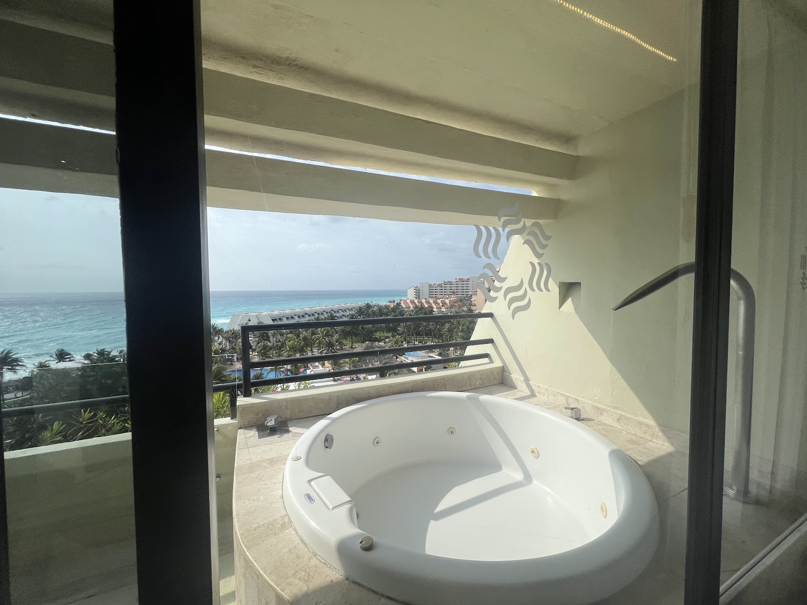 Whirlpool tub on a beachfront balcony at Grand Oasis Cancún overlooking the turquoise Caribbean Sea and palm-lined shore.