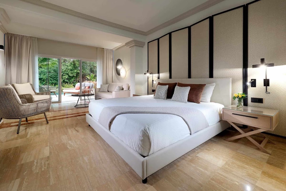 Modern bedroom at Grand Palladium Jamaica with white bed, sitting area, and garden view through sliding glass doors.