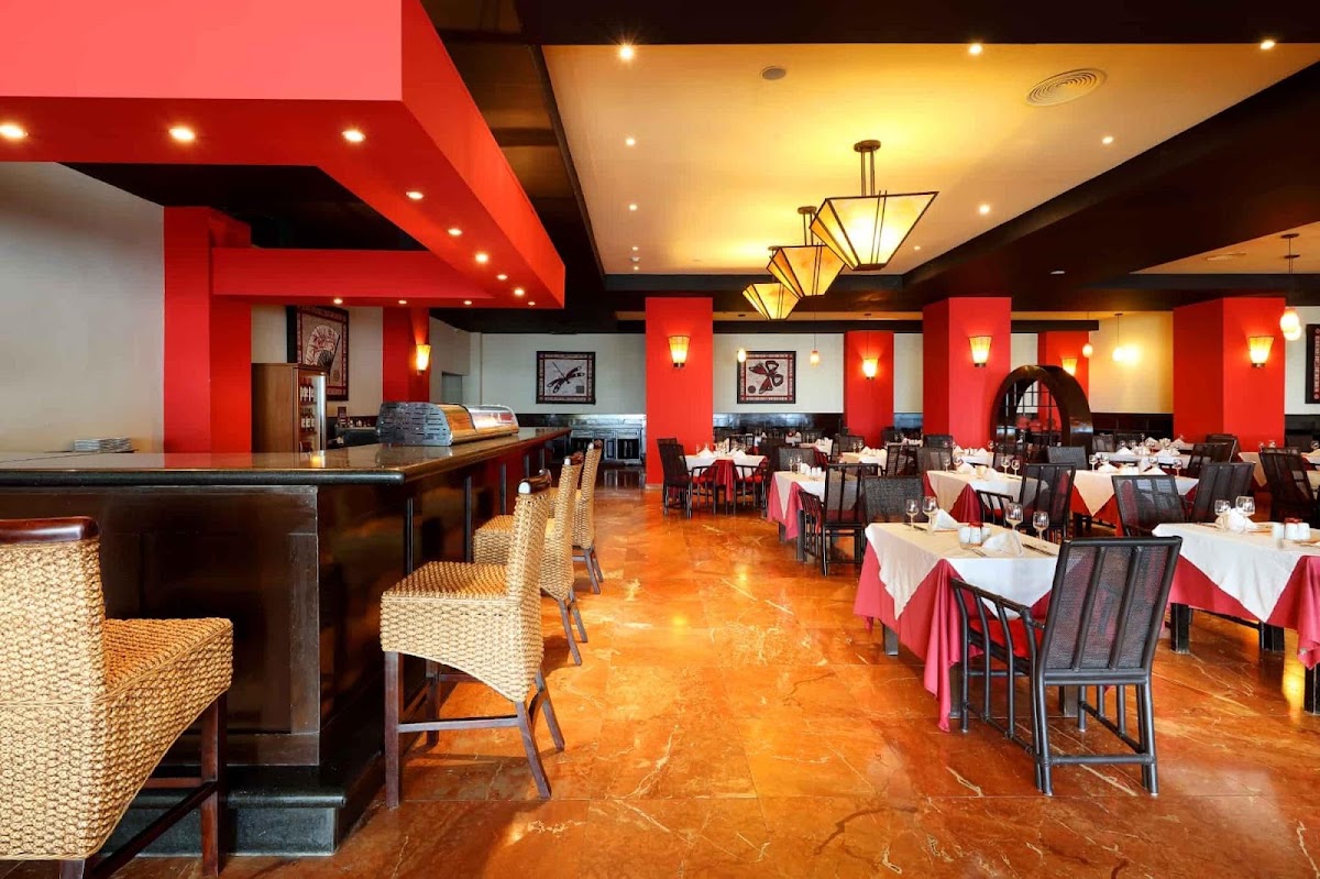 Restaurant dining room with red pillars, white-clothed tables, bar counter on left, and polished orange-brown floor.