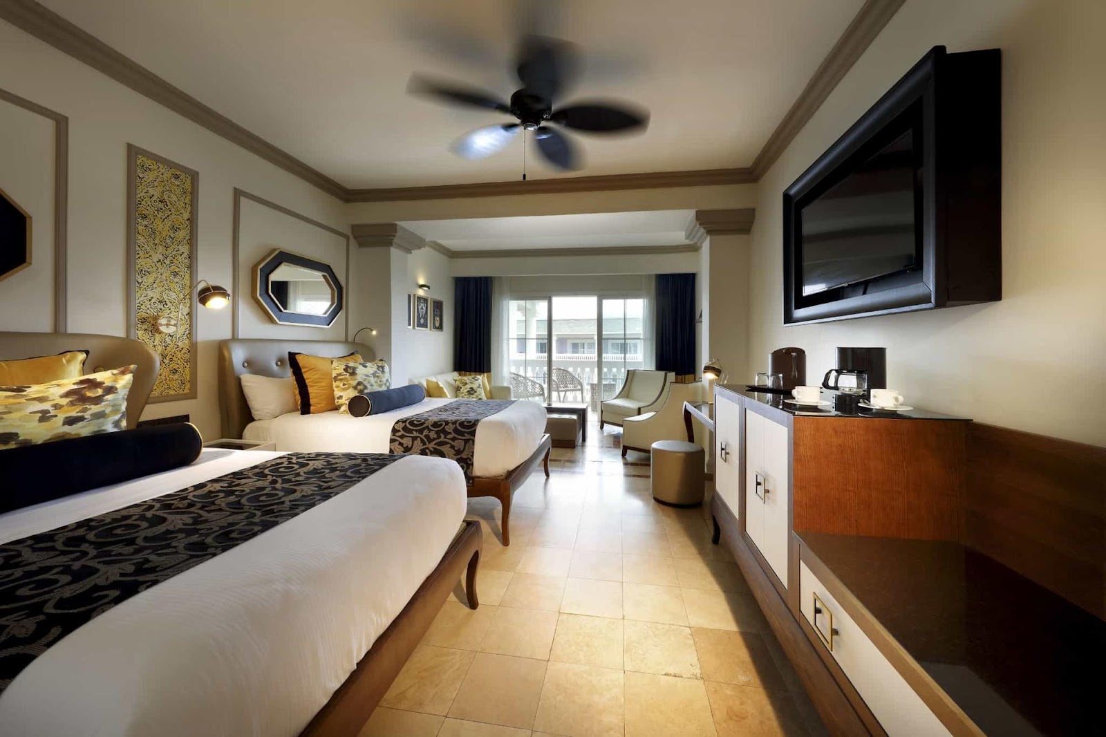 Spacious resort room with two queen beds, gold and navy accents, wall-mounted TV, and balcony overlooking the property at Grand Palladium Lady Hamilton.