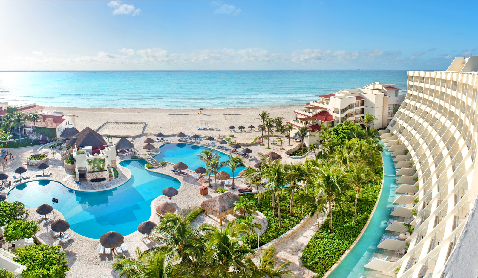 Aerial view of Grand Park Royal Cancún with lagoon-style pools, thatched umbrellas, palm trees, and beachfront overlooking turquoise Caribbean waters.