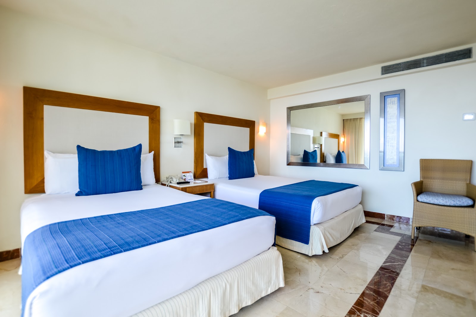 Resort guest room with two queen beds dressed in white linens and blue runners, wooden headboards, and blue accent pillows.