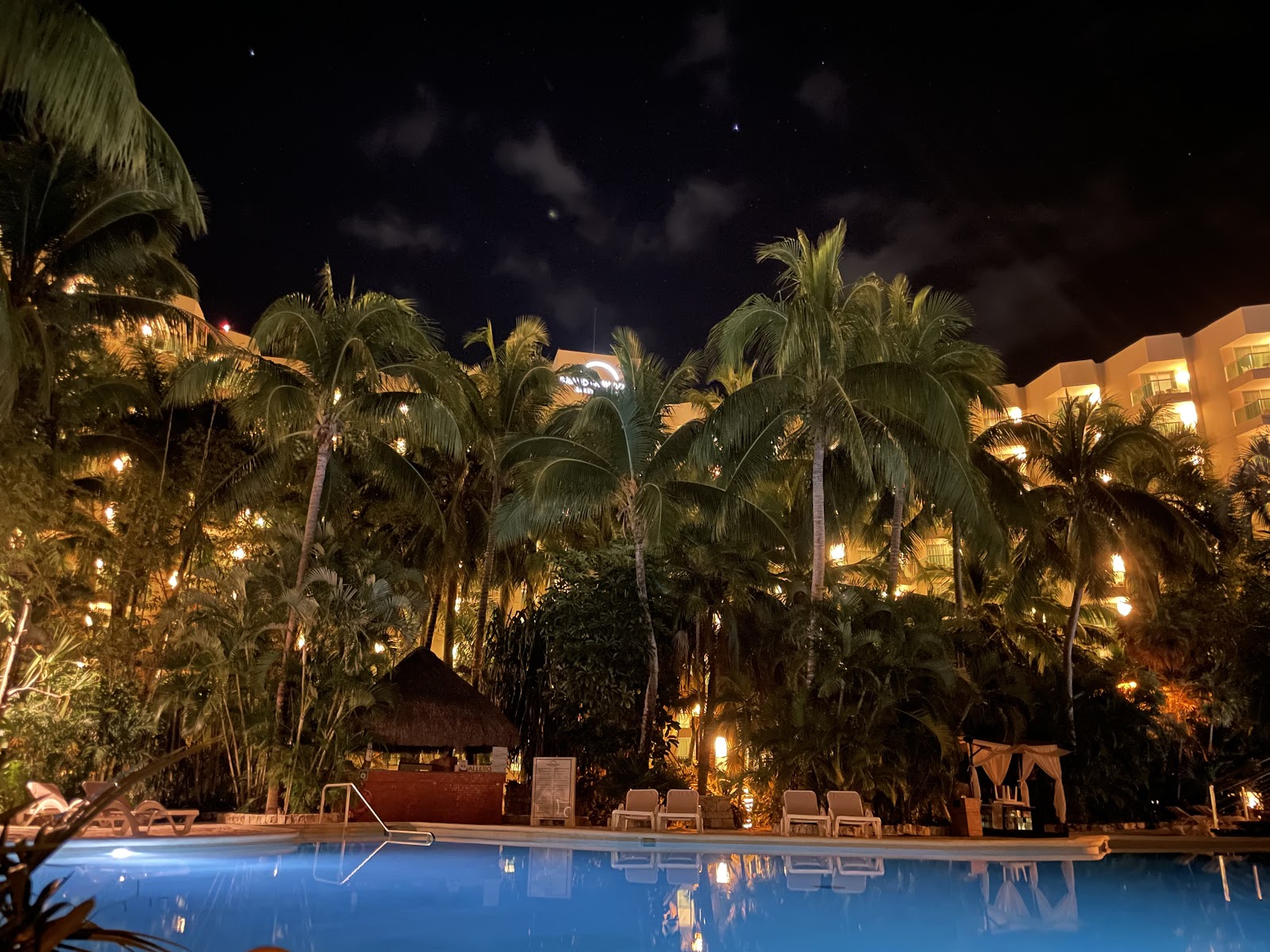 Turquoise lagoon pool surrounded by stone structures and palm trees at Grand Park Royal Cozumel, with resort buildings visible in the background.