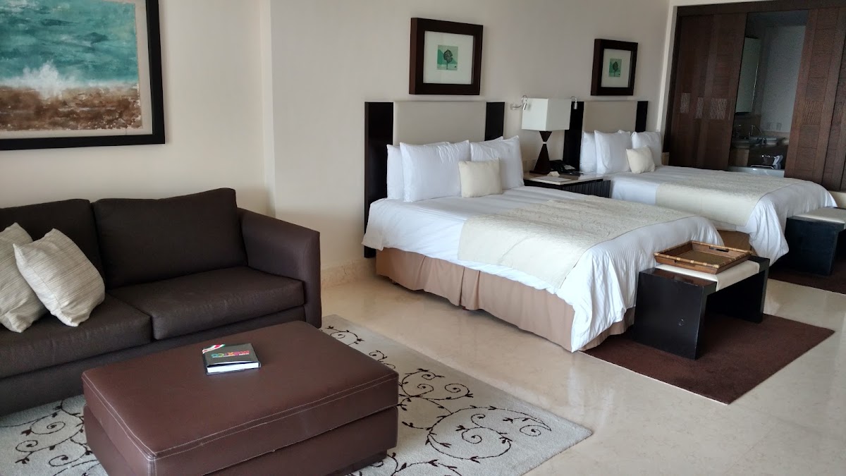 Spacious resort room with two queen beds, brown leather sofa, and framed ocean artwork at Grand Velas Riviera Maya.