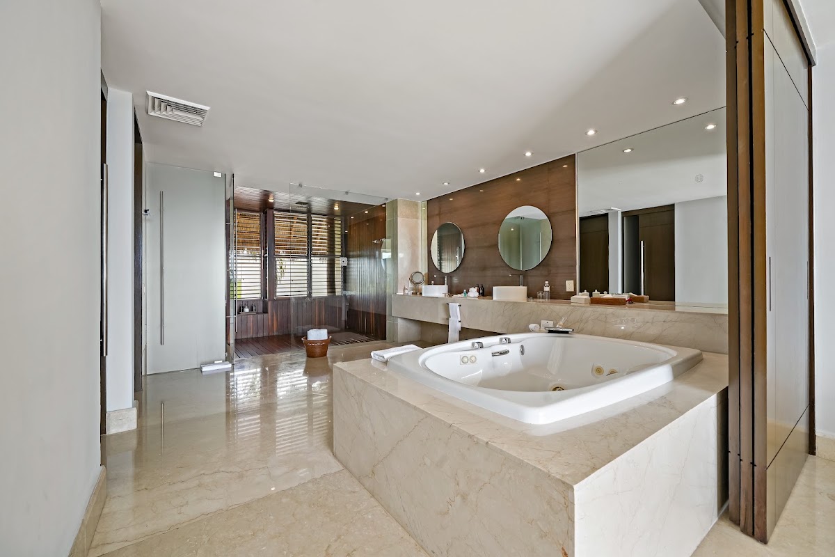Spacious bathroom with marble soaking tub, dual vanity with round mirrors, wood accents, and glass-enclosed shower at Grand Velas Riviera Maya.