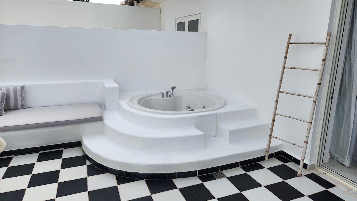 Bathroom with sunken circular whirlpool tub, black-and-white checkered floor, white built-in bench seating, and wooden ladder at Grecotel Caramel Boutique Resort.