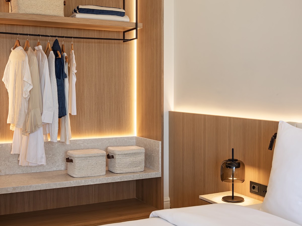 Wood-paneled closet area with hanging clothes, woven storage baskets, and warm ambient lighting in a modern resort room.