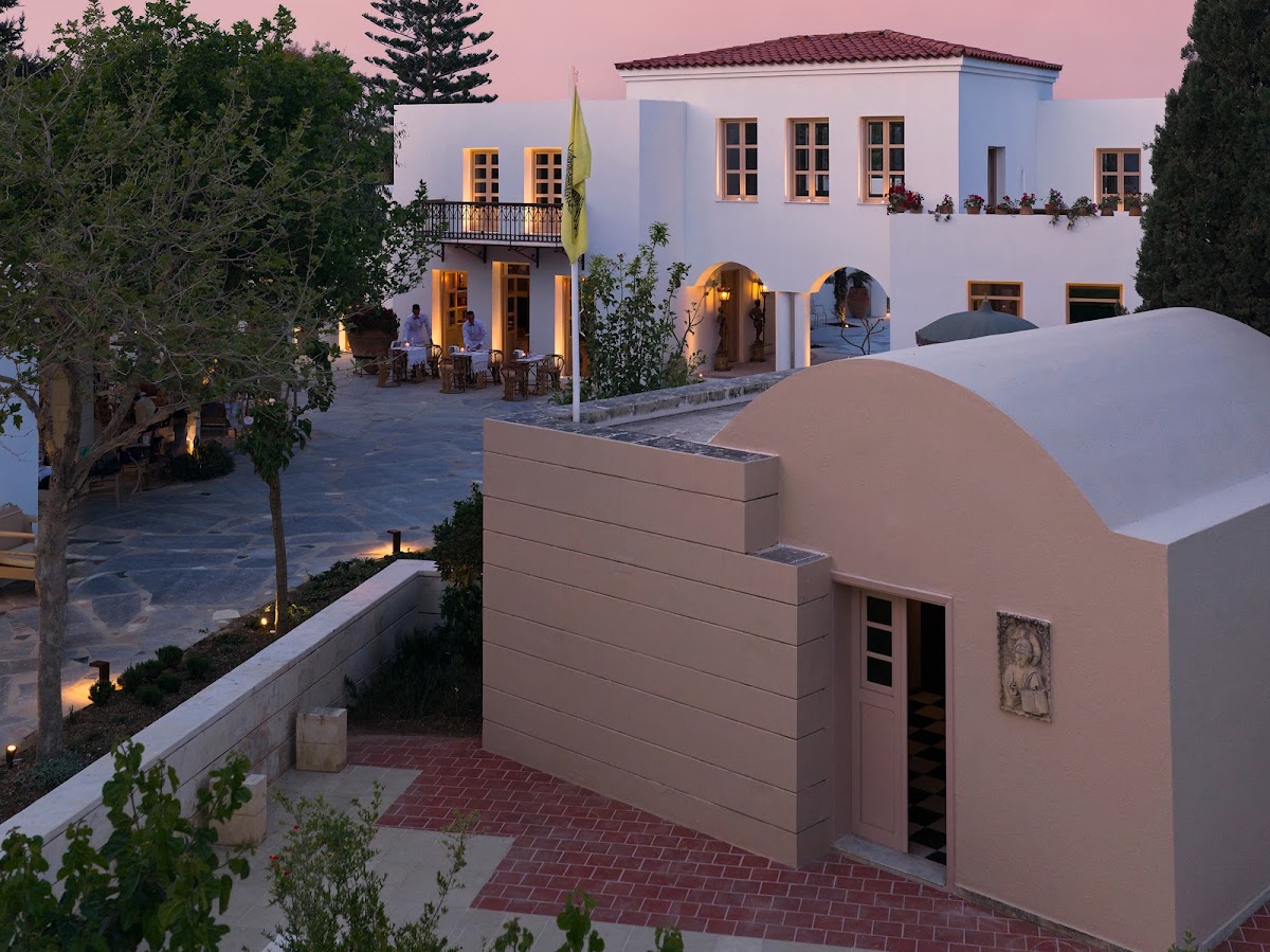 White Mediterranean villa with arched doorways and lit windows at dusk, guests dining on a courtyard terrace beyond.