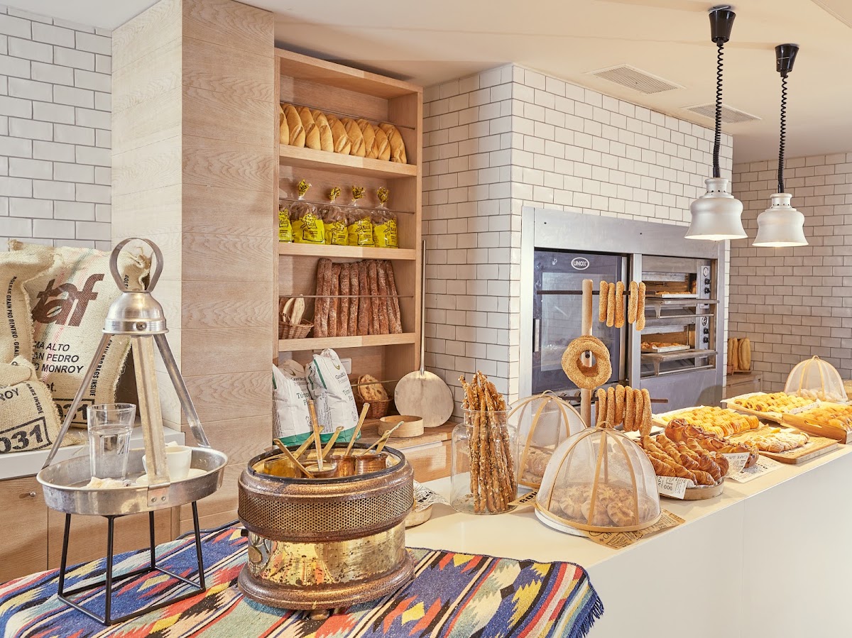 Resort bakery display with fresh breads, pastries, and baked goods on counter and wooden shelves, industrial ovens visible in background.
