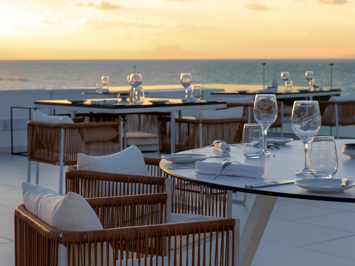 Outdoor dining tables set with glasses and place settings at sunset, overlooking the sea from a clifftop terrace at Grecotel LUXME White.