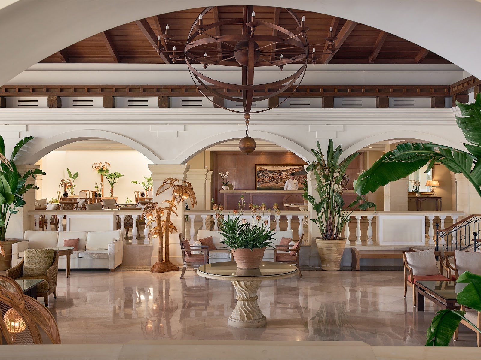 Elegant lobby with arched ceilings, ornate chandelier, potted plants, and seating areas overlooking a reception desk.