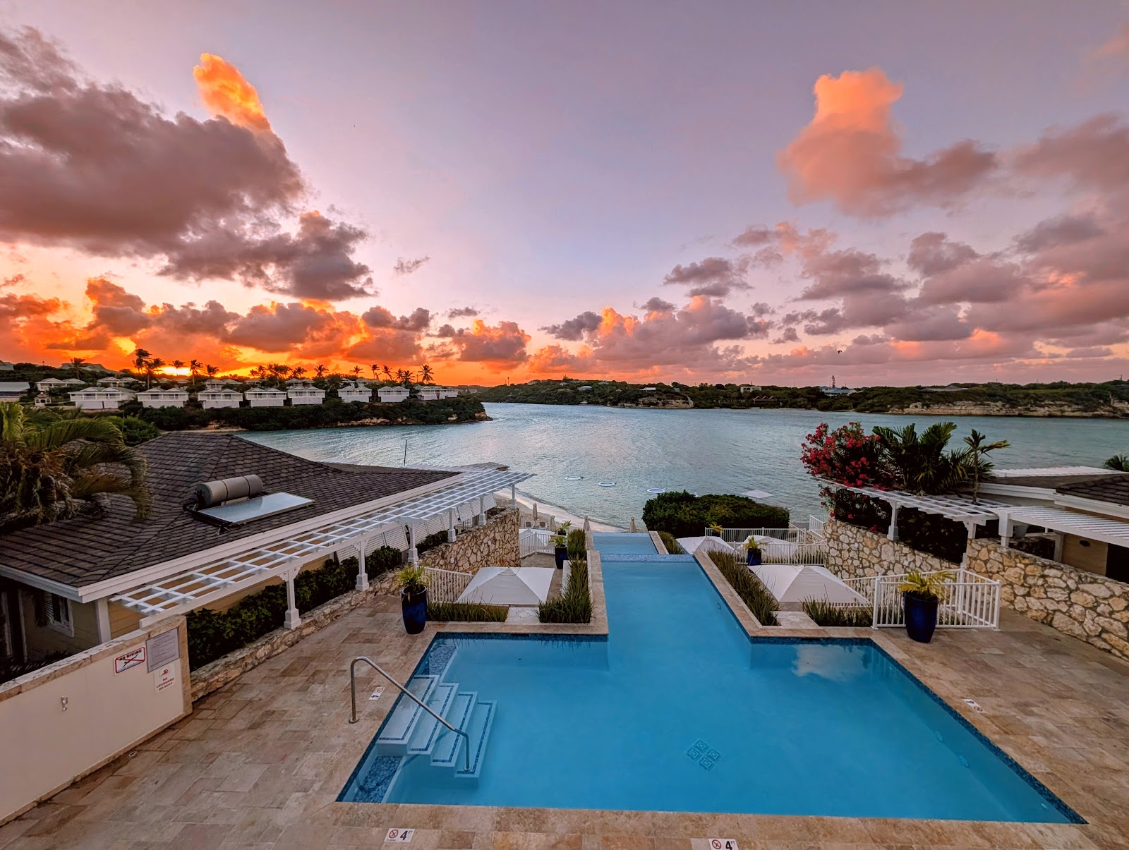 Resort swimming pool overlooking turquoise bay at sunset with palm trees and oceanfront bungalows at Hammock Cove Antigua.