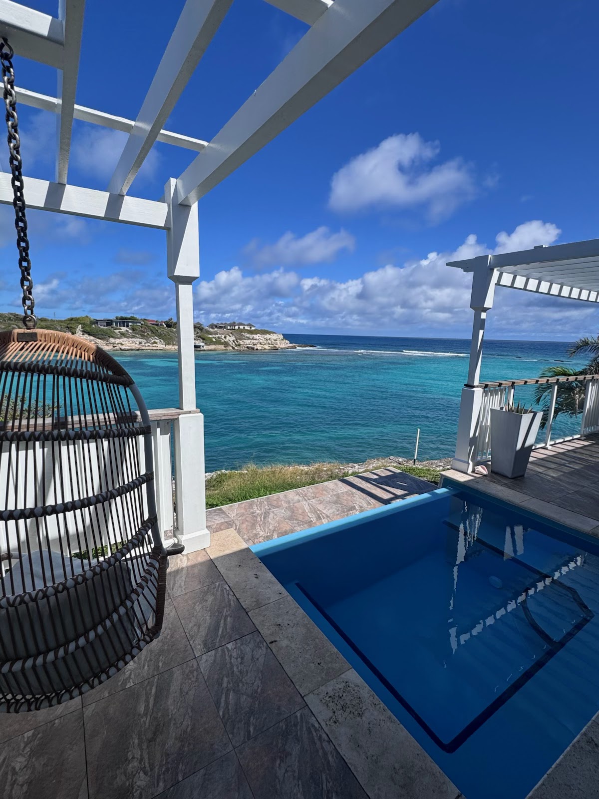 White buildings with a central cupola sit on a rocky peninsula overlooking turquoise water at Hammock Cove Antigua.