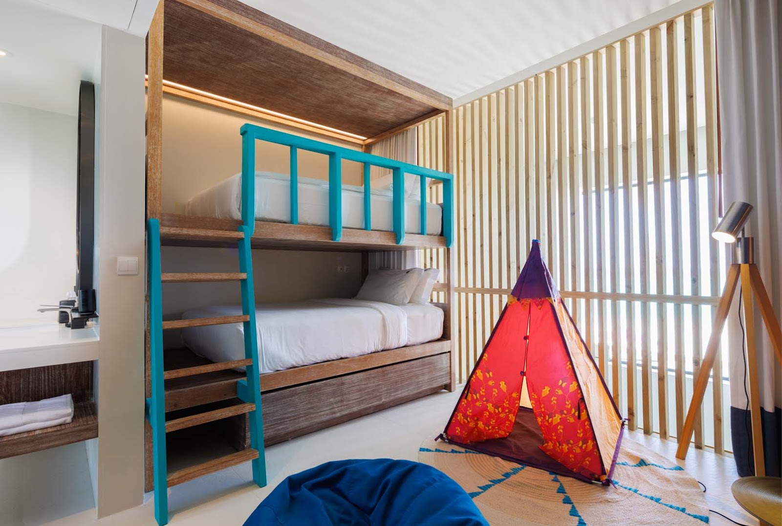 Kids' room with turquoise and wood bunk bed, red patterned teepee tent, blue floor cushion, and slatted room divider at Hard Rock Hotel Maldives.