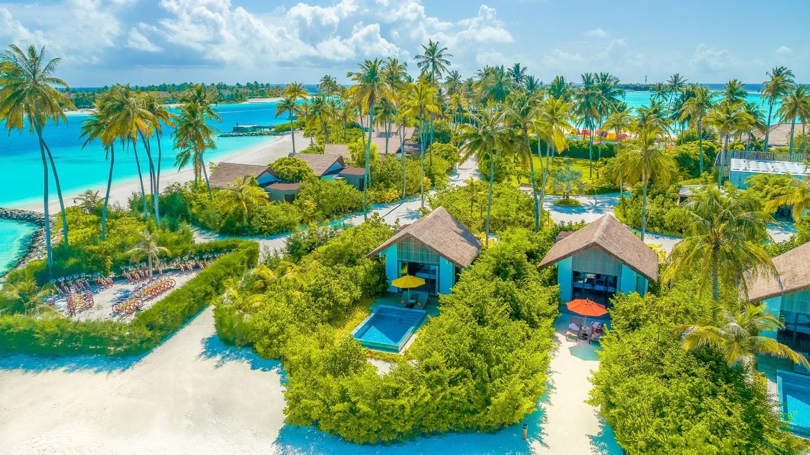 Aerial view of Hard Rock Hotel Maldives with turquoise lagoons, thatched-roof bungalows nestled among palms, white sand beaches, and multiple pools.