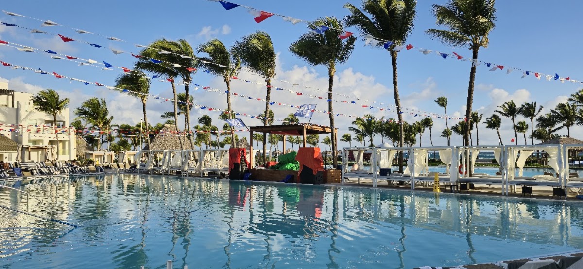 Resort pool with colorful bunting strung overhead, palm trees, white cabanas, and a red play structure in the water at Hard Rock Hotel & Casino Punta Cana.
