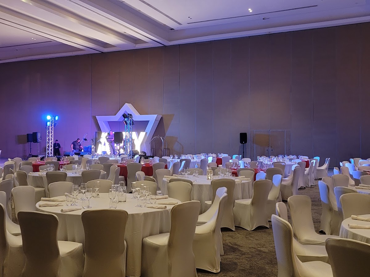 Ballroom with round tables covered in white linens, cream-colored chair covers, and a stage with illuminated star backdrop and blue lighting at Hard Rock Hotel & Casino Punta Cana.
