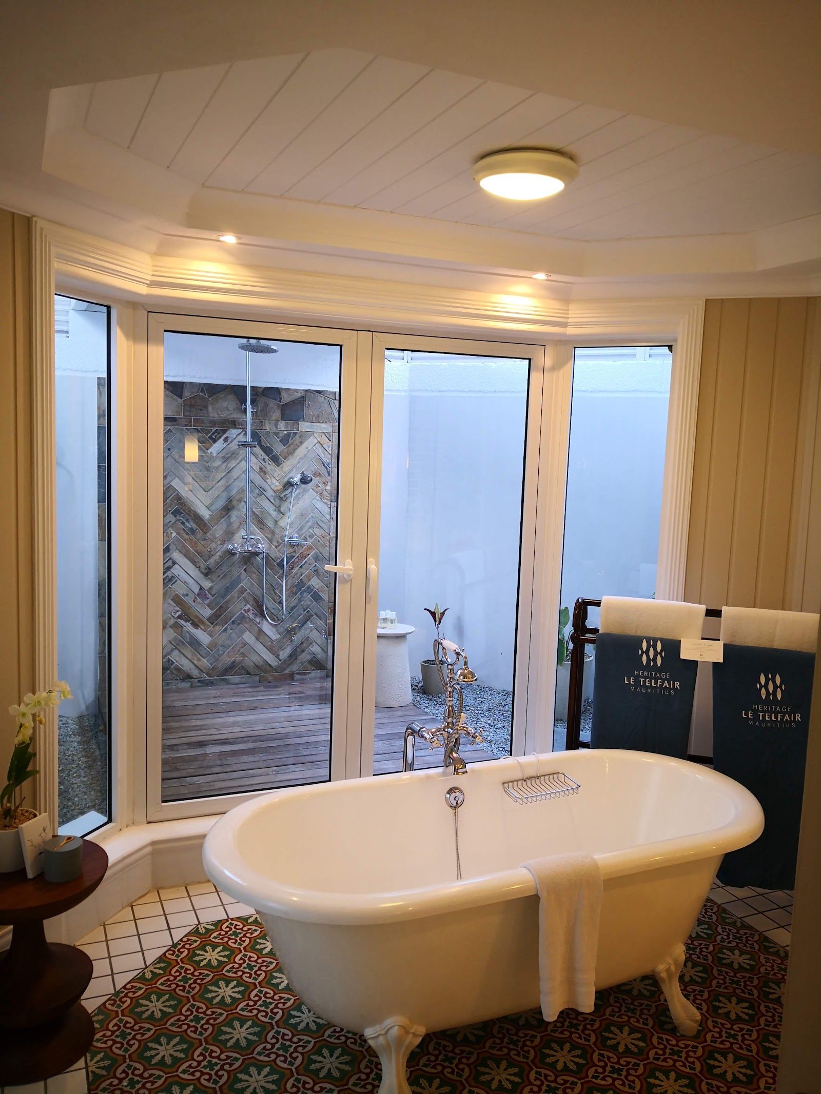 Freestanding soaking tub in a luxury bathroom with glass shower enclosure and doors opening to an outdoor courtyard at Heritage Le Telfair.