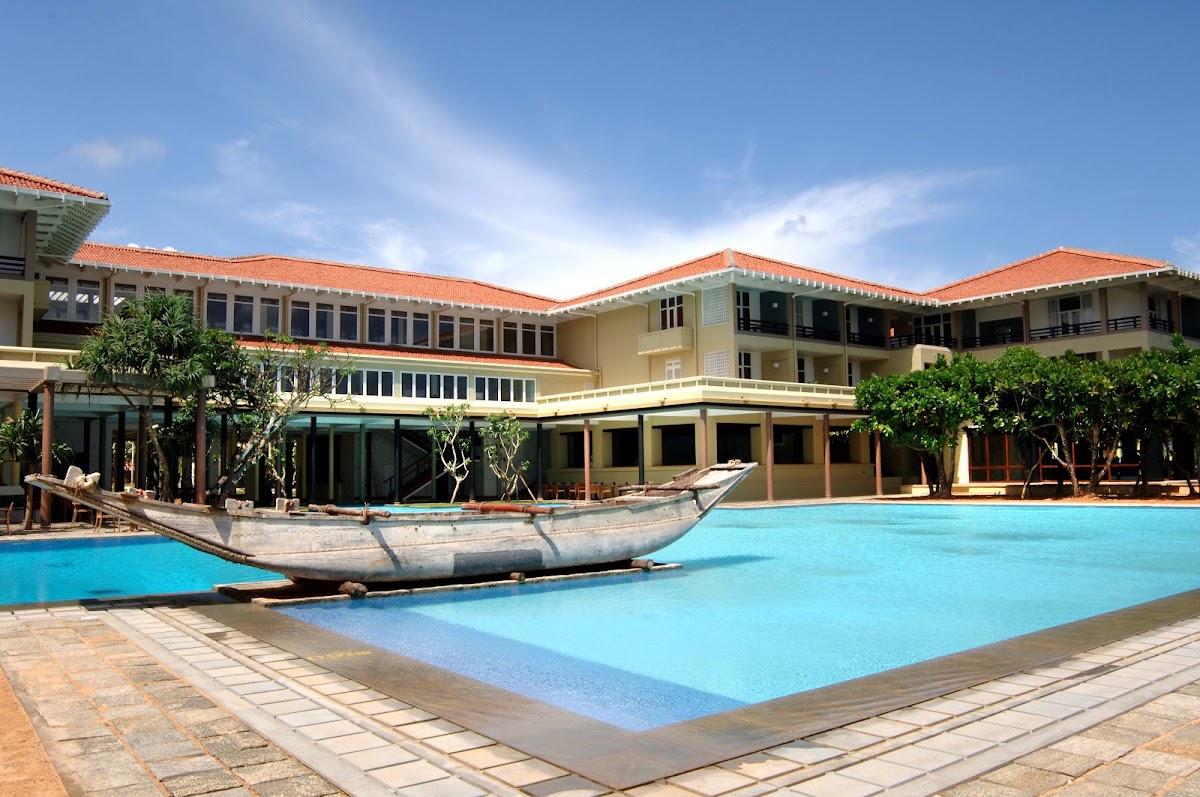 A wooden fishing boat sits in the center of a large turquoise pool at Heritance Ahungalla, with cream and orange colonial-style buildings surrounding the courtyard.