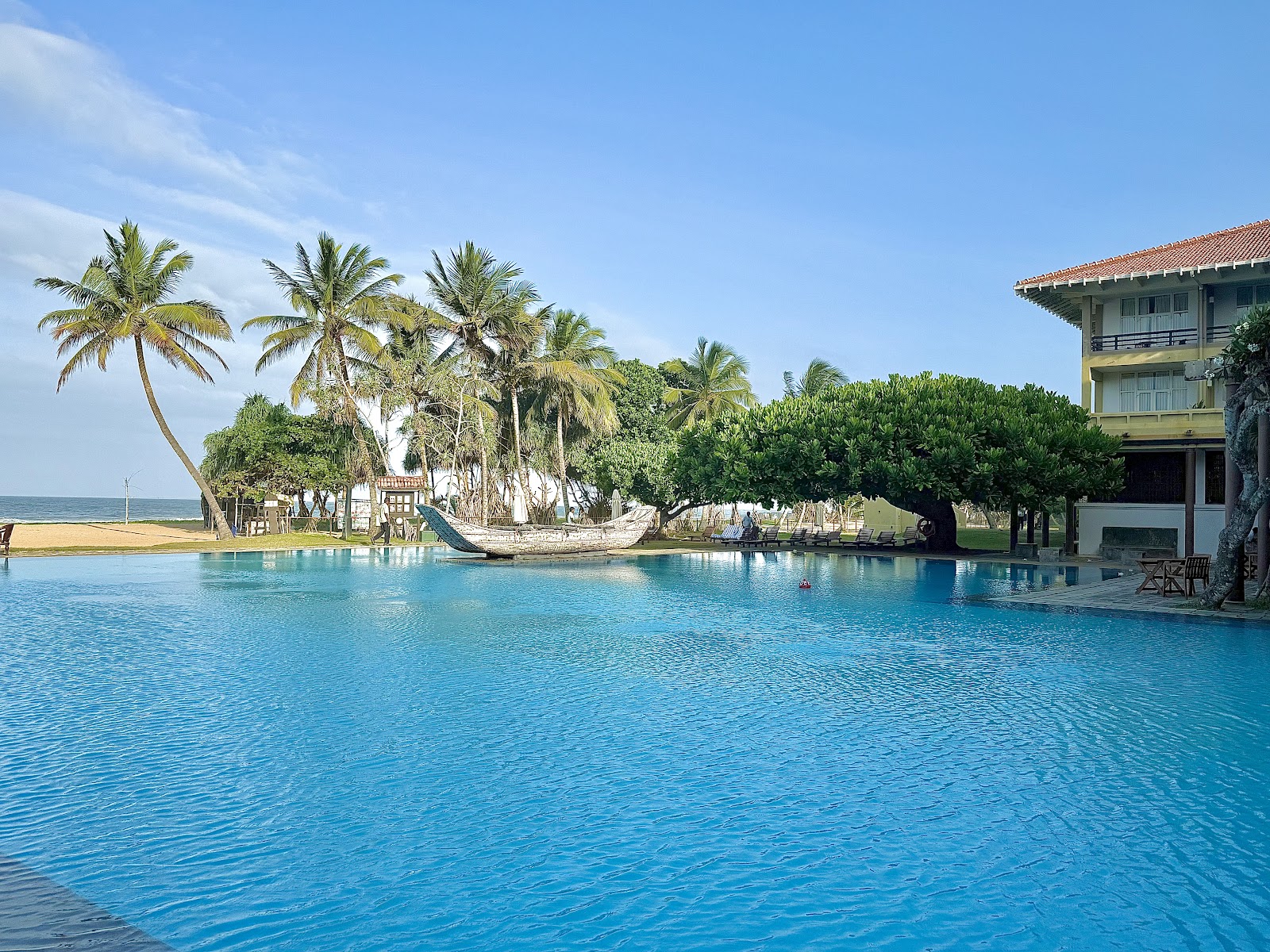 Infinity pool flowing toward the ocean at Heritance Ahungalla, with palm trees and sandy beach beyond.