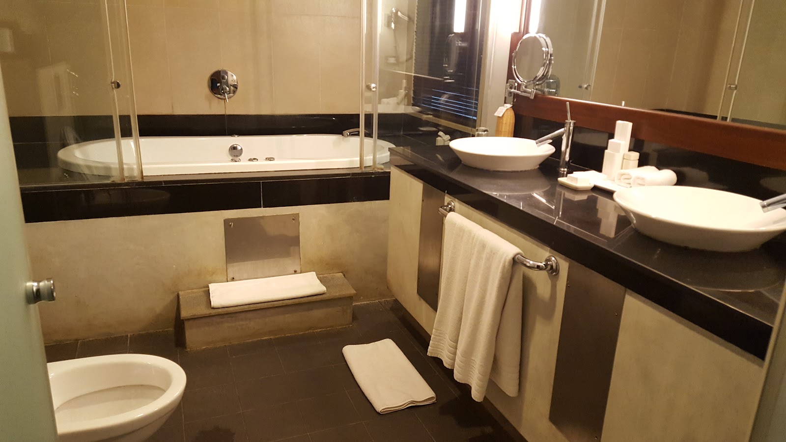 Bathroom at Heritance Ahungalla with soaking tub, double vessel sinks, and dark tile floors with cream walls.
