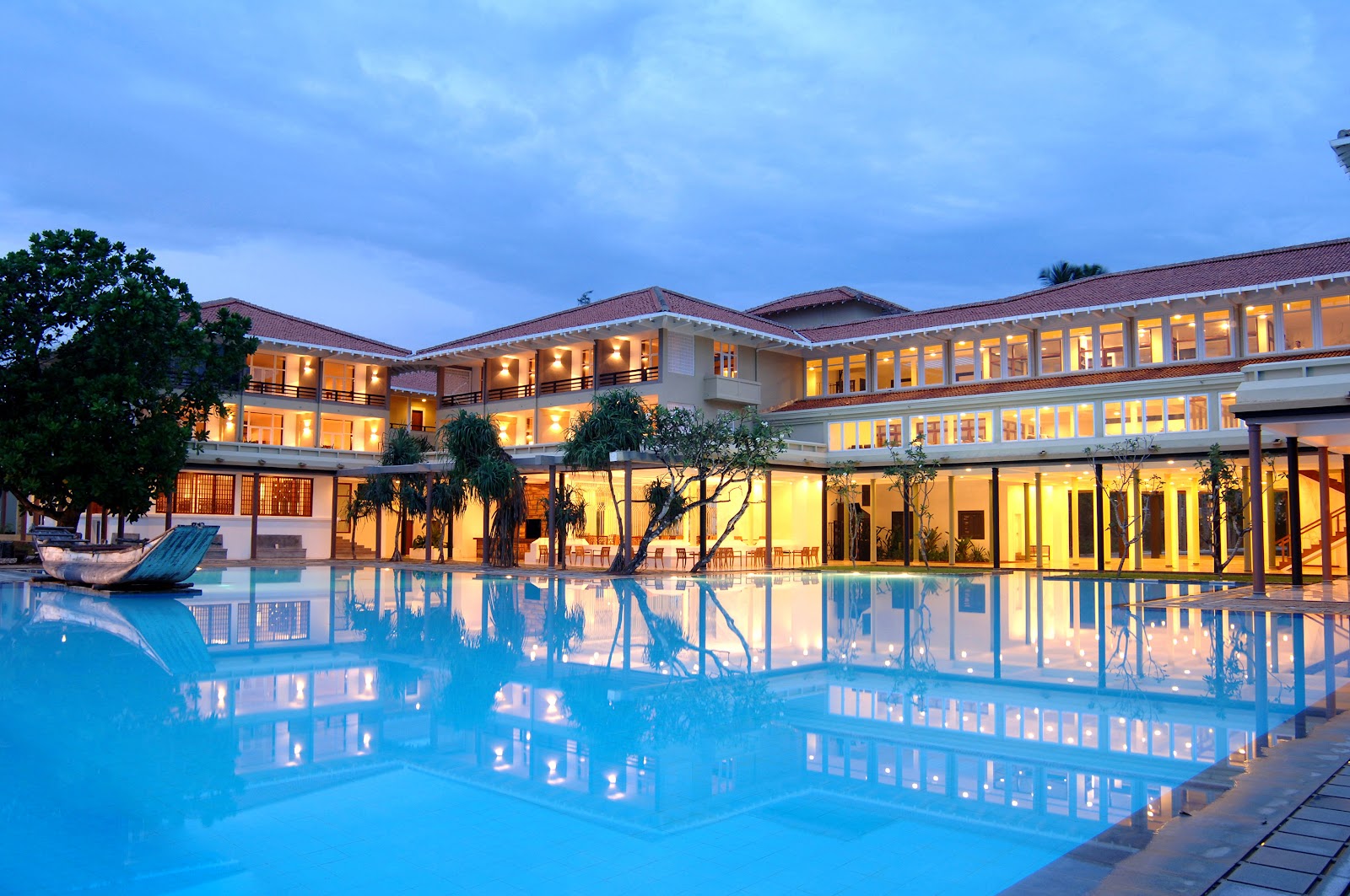 Heritance Ahungalla's lit main building and pool at dusk, with palm trees reflected in the blue water.