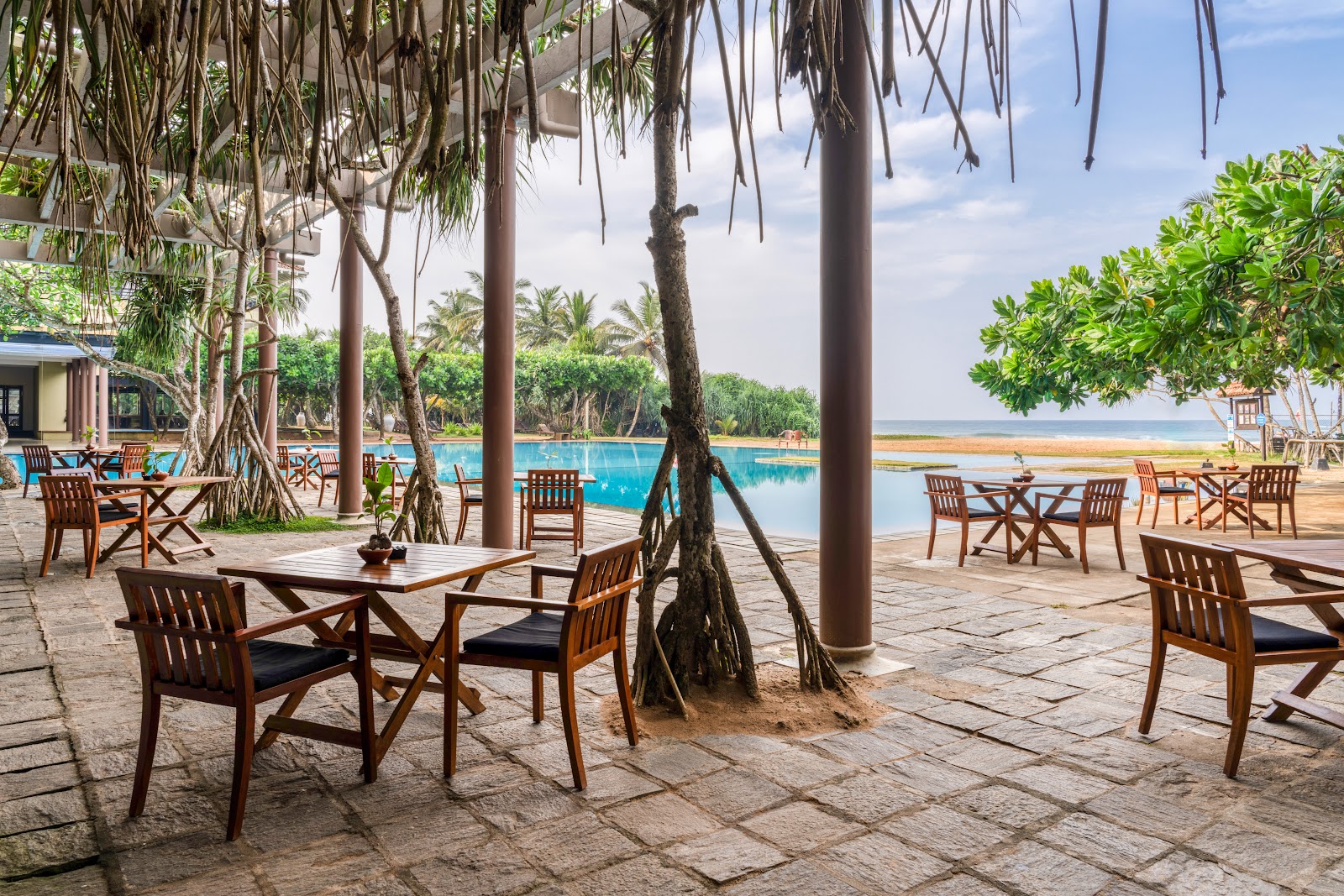 Illuminated pool at dusk overlooking a sandy beach and ocean at Heritance Ahungalla, with palm trees and lounge chairs surrounding the water.