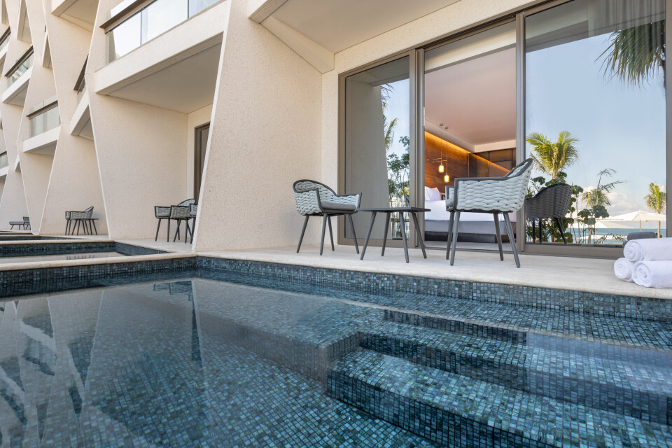 Private plunge pool with tiled steps beside a modern suite terrace featuring lounge chairs, potted palms, and ocean views at Hilton Cancun.