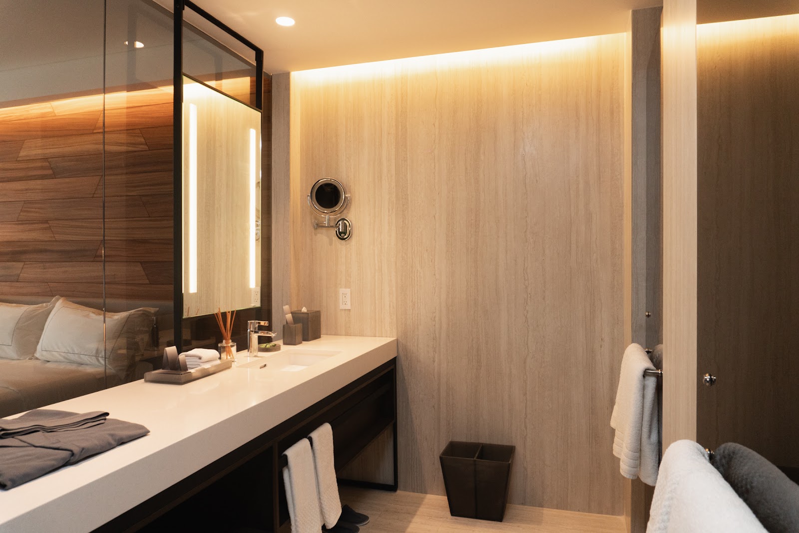 Modern bathroom with illuminated mirror, white countertop, wood-grain walls, and soaking tub at Hilton Cancun.